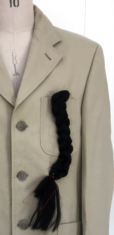 Integrating hair with garments. Fake black braid on the pocket of beige men's jacket.