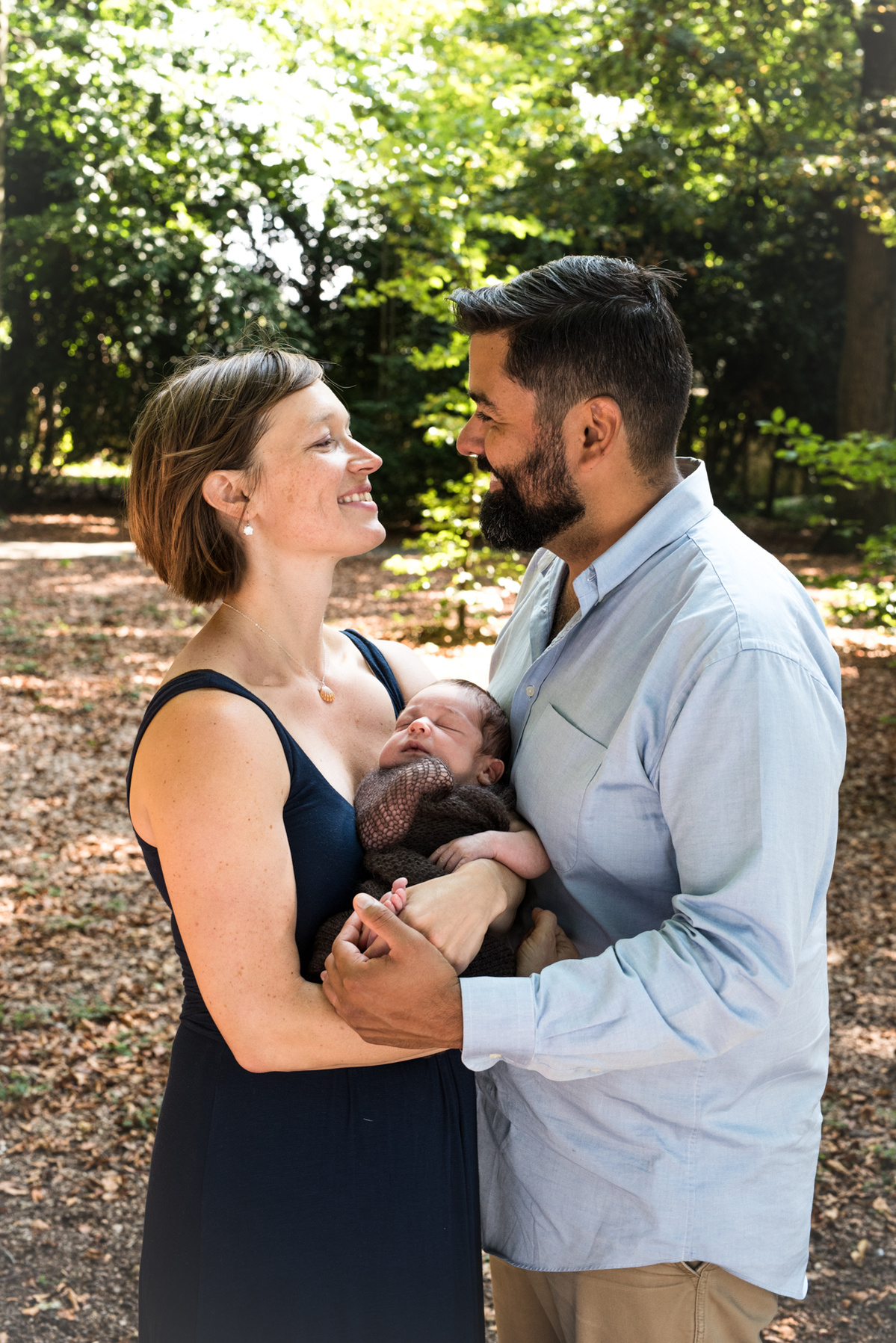 Face to face, both parents look into each other's eyes, gloriously happy, holding their newborn son in their arms. Family and newborn photographer, Chene-Bougeries.