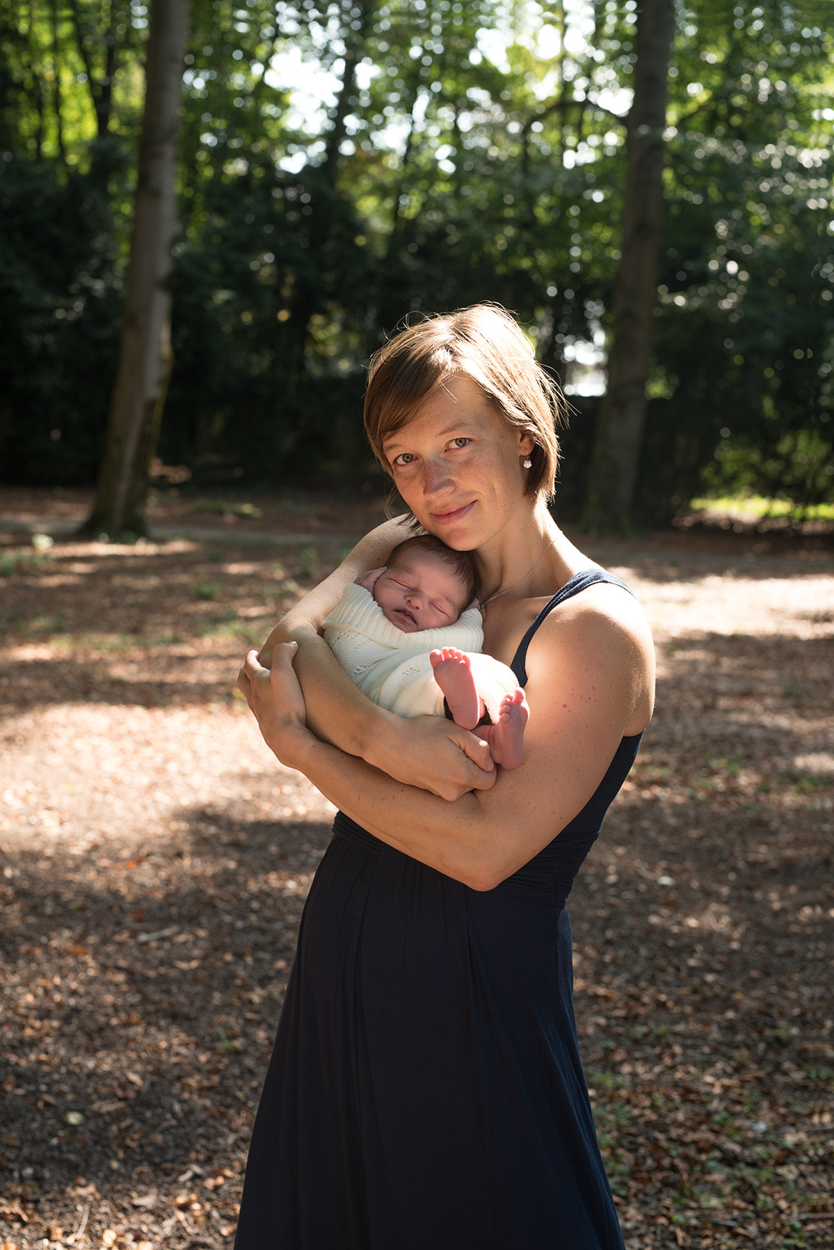 Proud loving mother poses for a professional portrait of herself cradling her newborn son, shot in the parc des Eaux-Vives, Geneva, by Helen Putsman, family and newborn photographer.