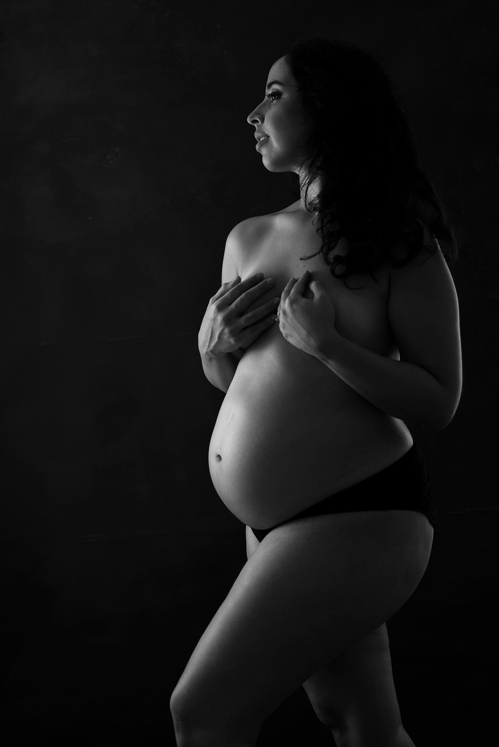 Fine-Art Maternity photographer based in Chêne-Bougeries, Geneva. Black and white dark nude maternity photo shot in the studio.  The pregnant belly is beautifully highlighted in black and white.