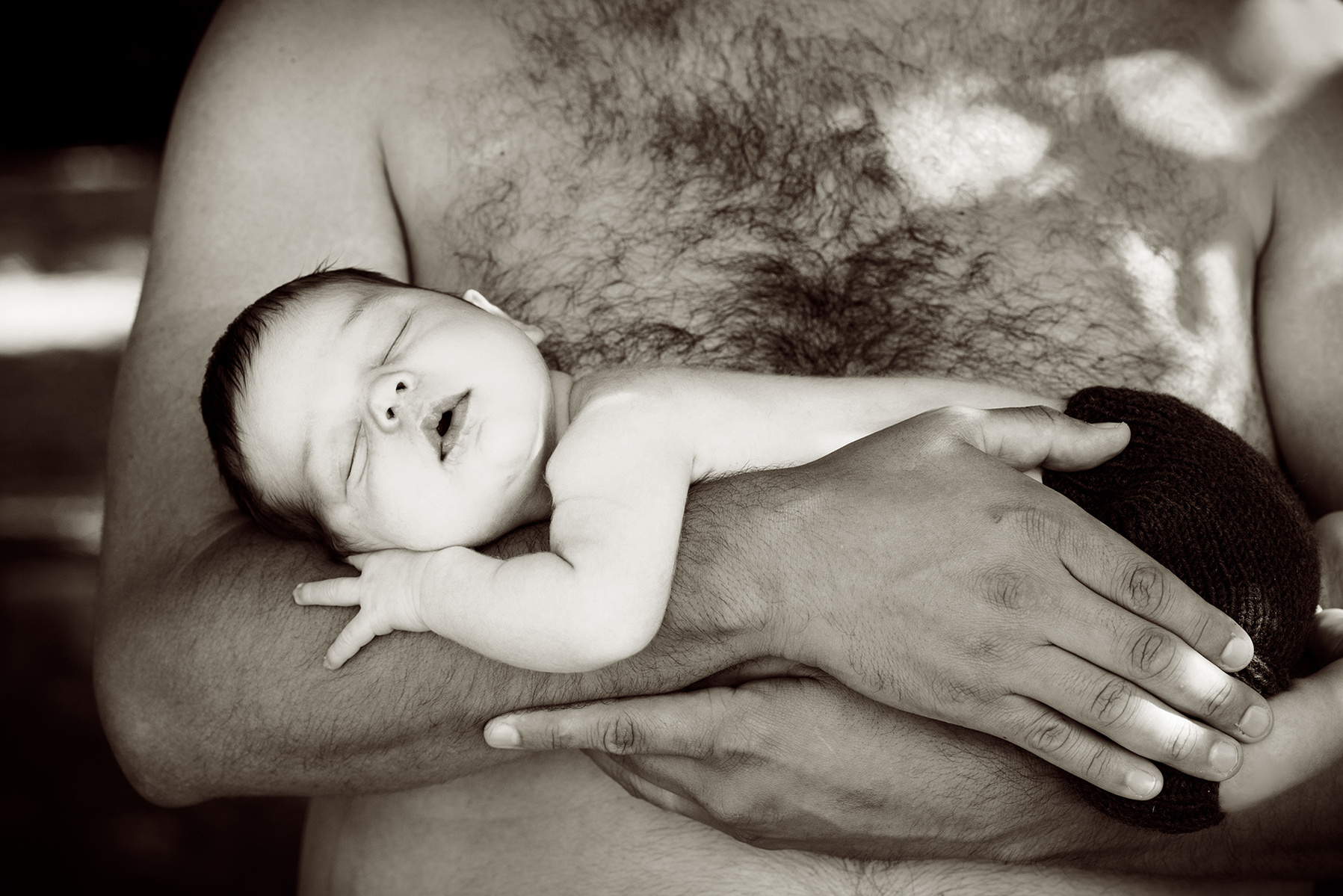 Close up black and white portrait of a bare-chested young loving father, holding his baby son in his arms. Family and newborn photographer, Helen Putsman, works from Chene-Bougeries, Geneva.