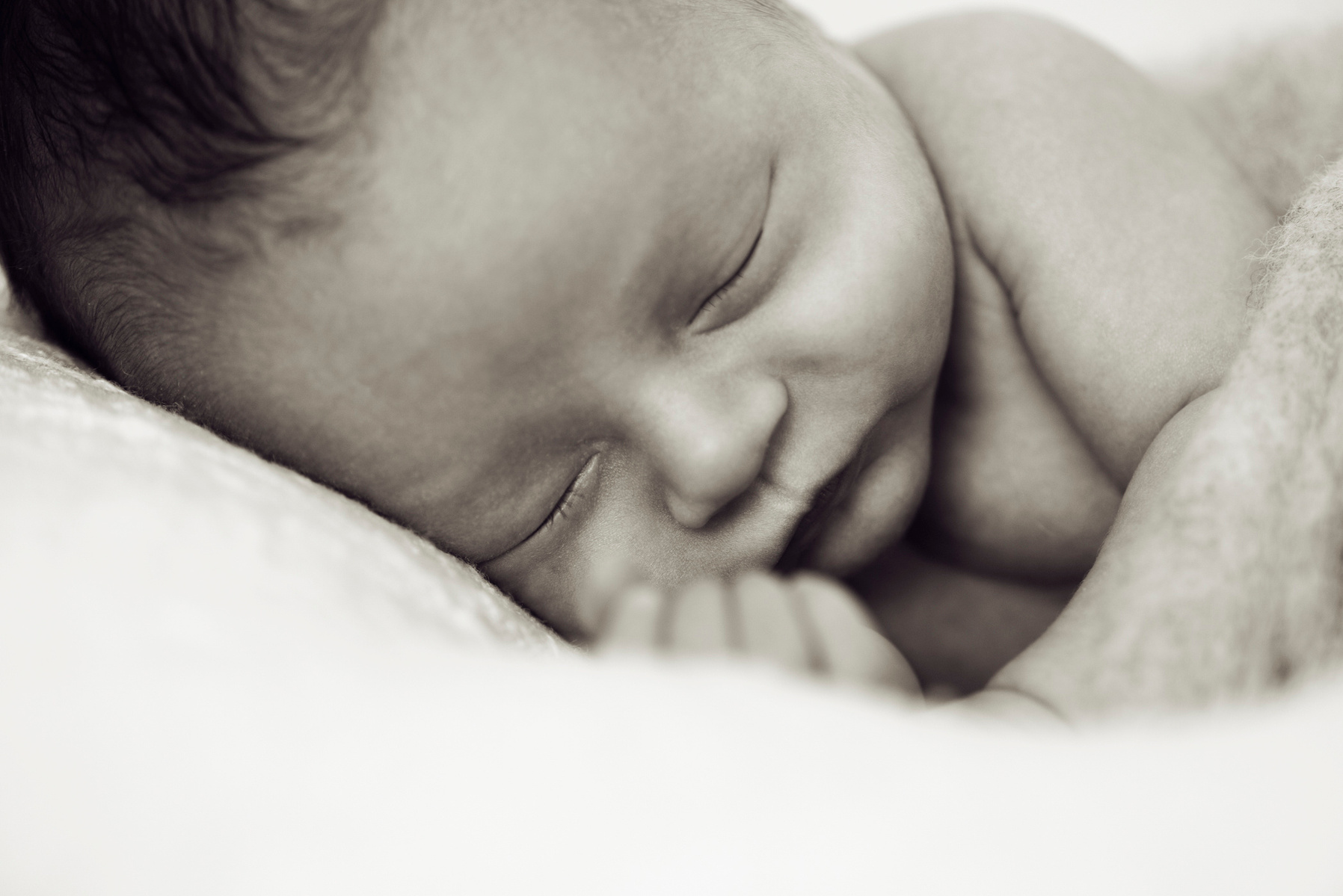 Black and white close-up of newborn baby boy's face, he was wrapped in felt sleeping on a white blanket, photographed by Helen Putsman, Geneva's leading family and newborn photographer. 