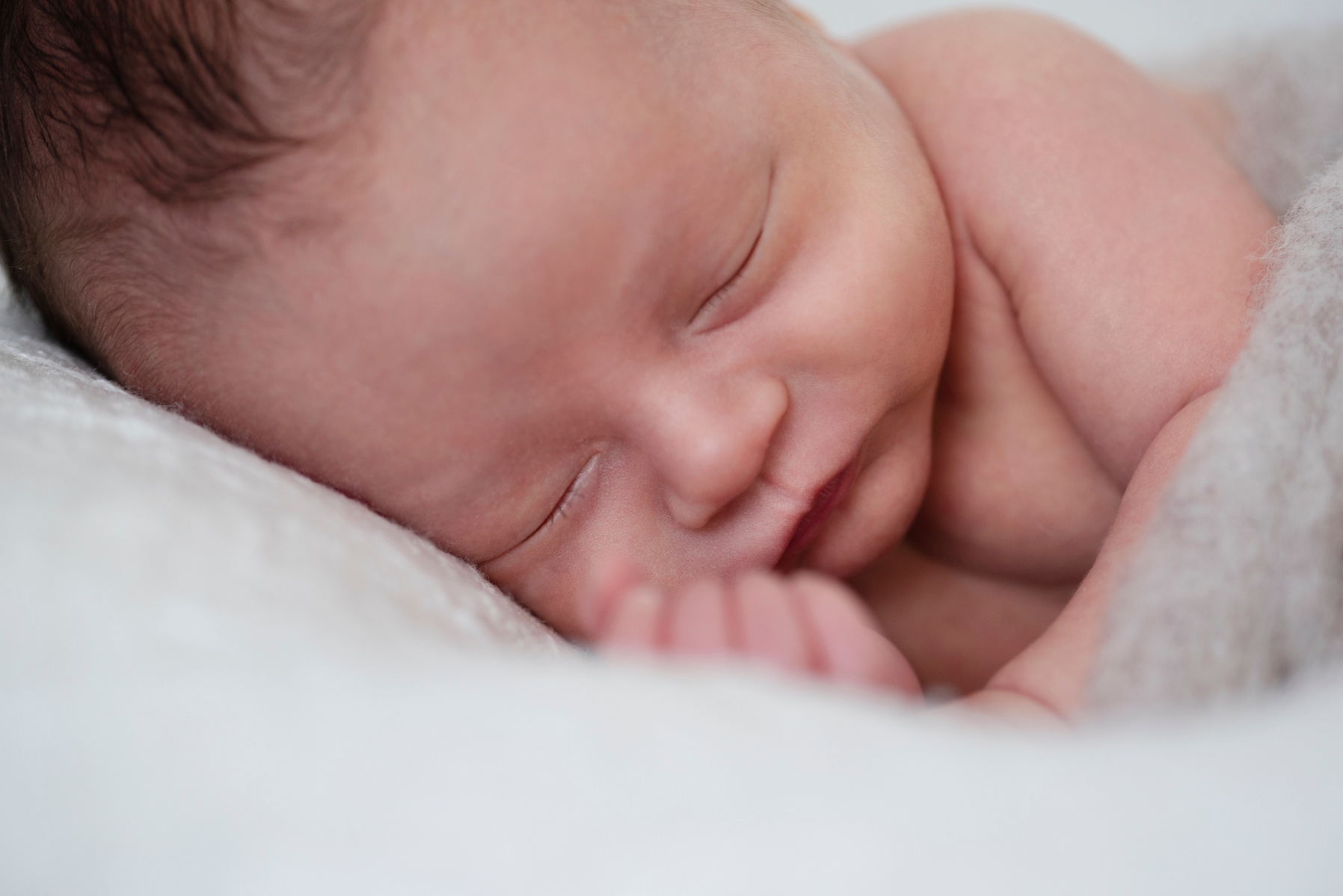 Close-up of newborn baby boy's face, he was wrapped in felt sleeping on a white blanket, photographed by Helen Putsman, Geneva's leading family and newborn photographer.