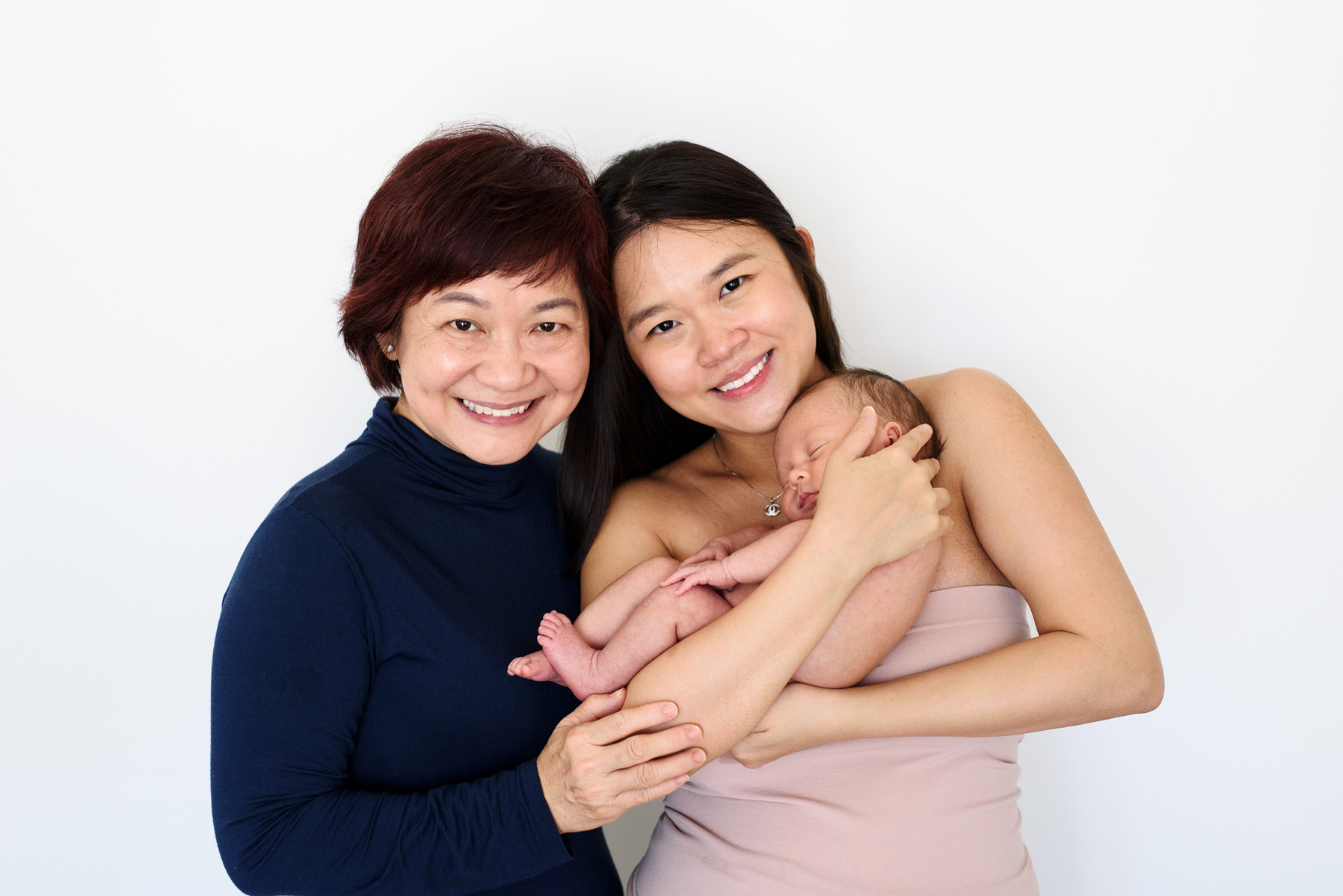 Three generations, the mother cradles her newborn son in her arms whilst the grandmother gets close for a happy family portrait. Photographed by Geneva's leading portrait photographer, Helen Putsman, based in Chêne-Bougeries.