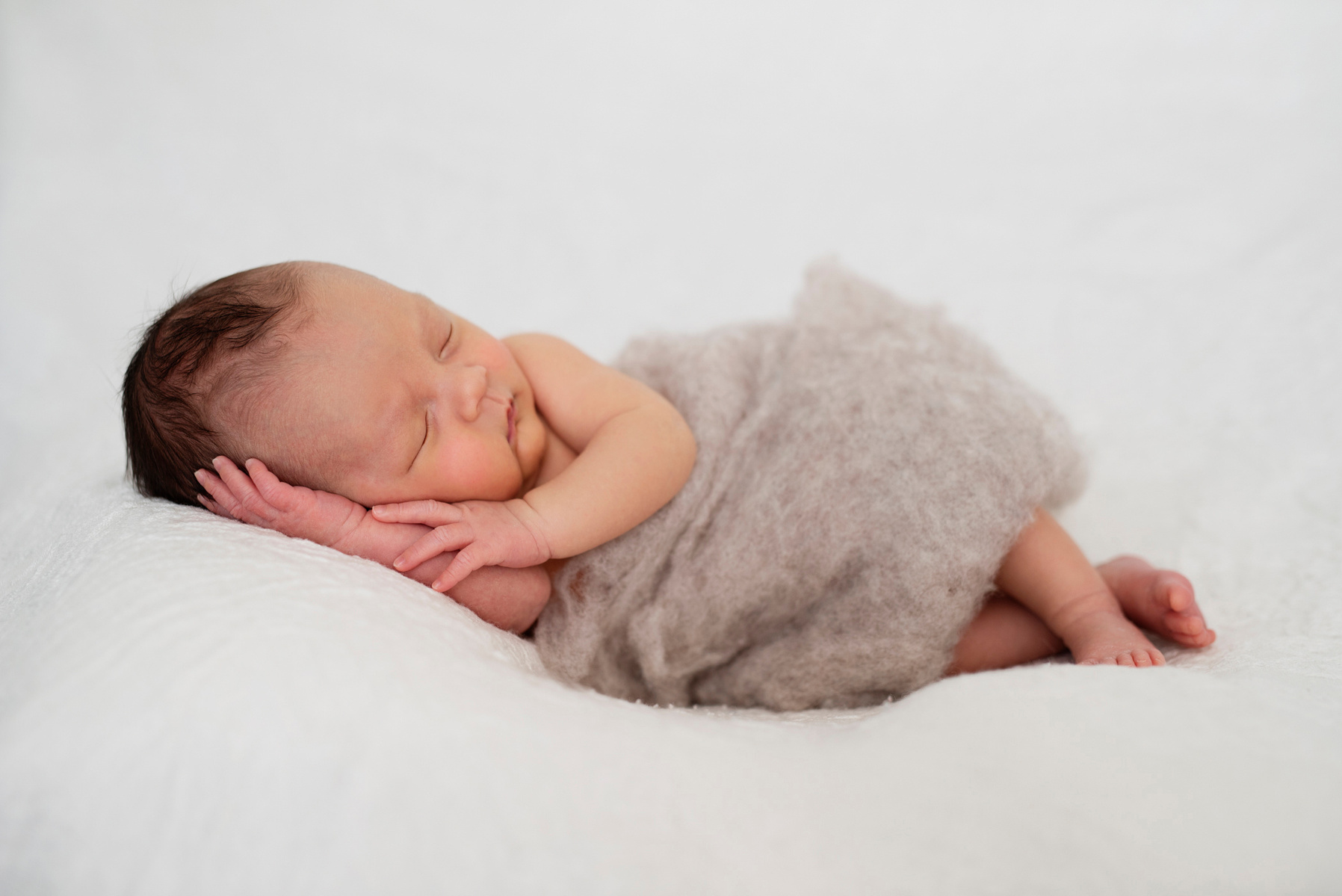 Newborn baby boy wrapped in felt sleeping on a white blanket, photographed by Helen Putsman, Geneva's leading family and newborn photographer.