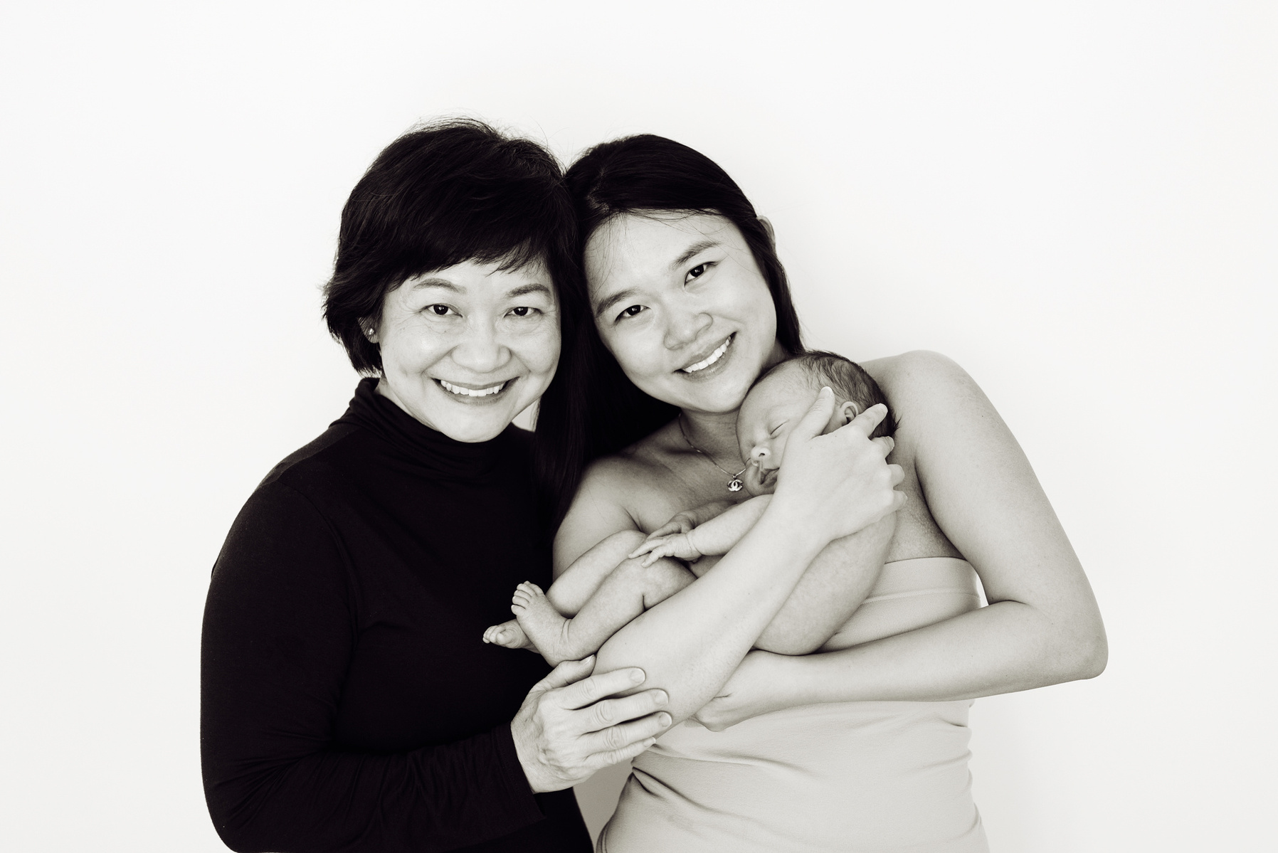 Three generations, the mother cradles her newborn son in her arms whilst the grandmother gets close for a professional family portrait with smiles. Photographed by Geneva's leading portrait photographer, Helen Putsman, based in Chêne-Bougeries.