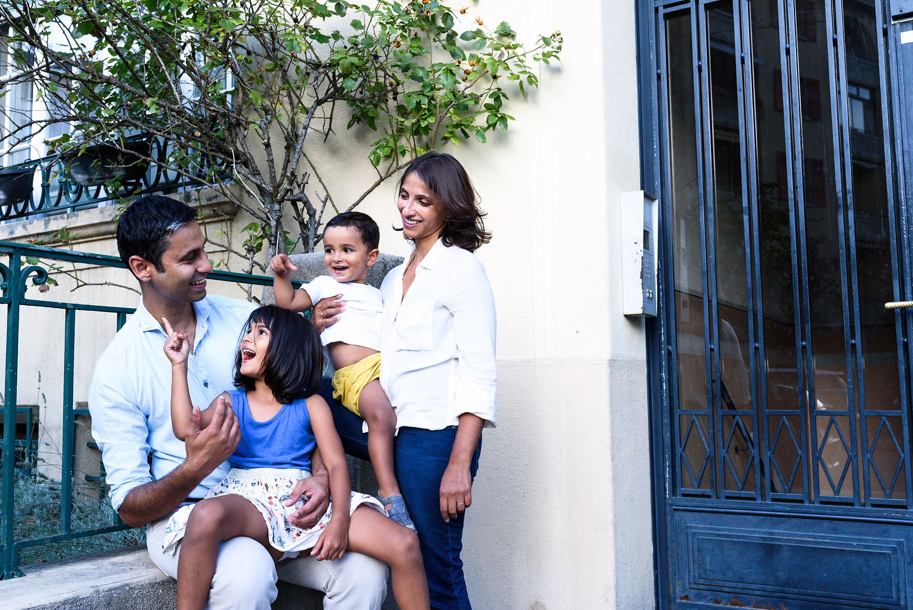 Family portrait shot outside the family flat with the daughter sitting on dad's lap and the mother holding her son in her arms. Shot in Geneva.