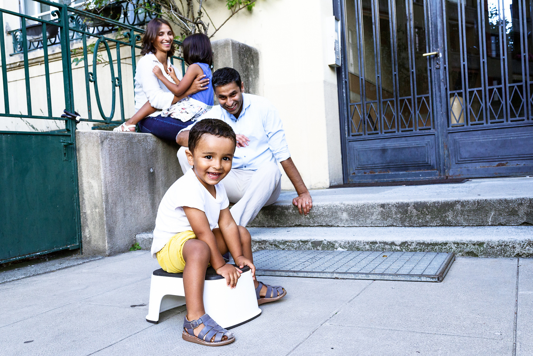 Reportage photo of the youngest of the family playing with the rest of the family in the background. Shot in Geneva, Switzerland.