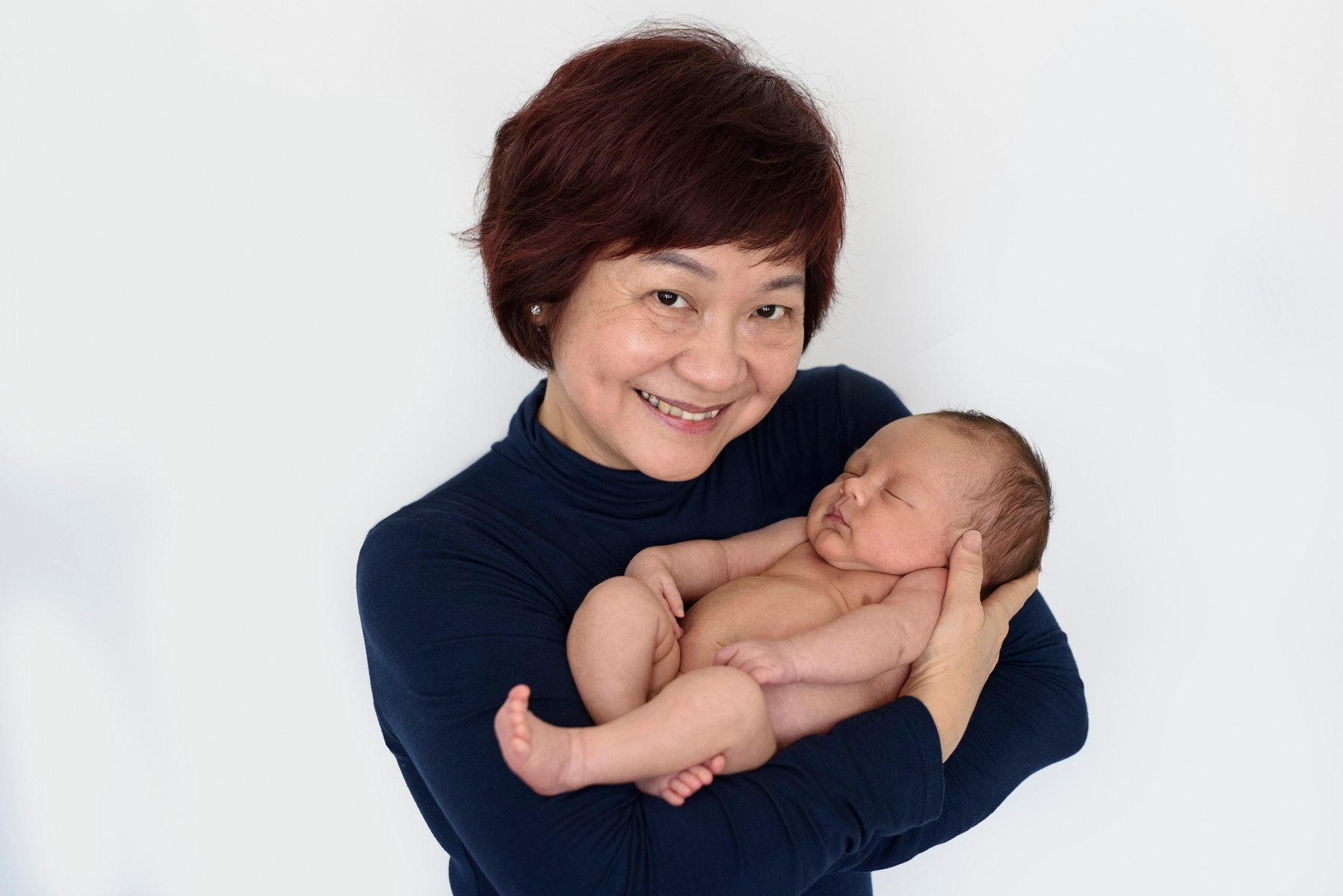 Grandmother cradles her newborn baby grandson in her arms for beautiful professional family portrait. Photographed by Geneva's leading portrait photographer, Helen Putsman, based in Chêne-Bougeries.
