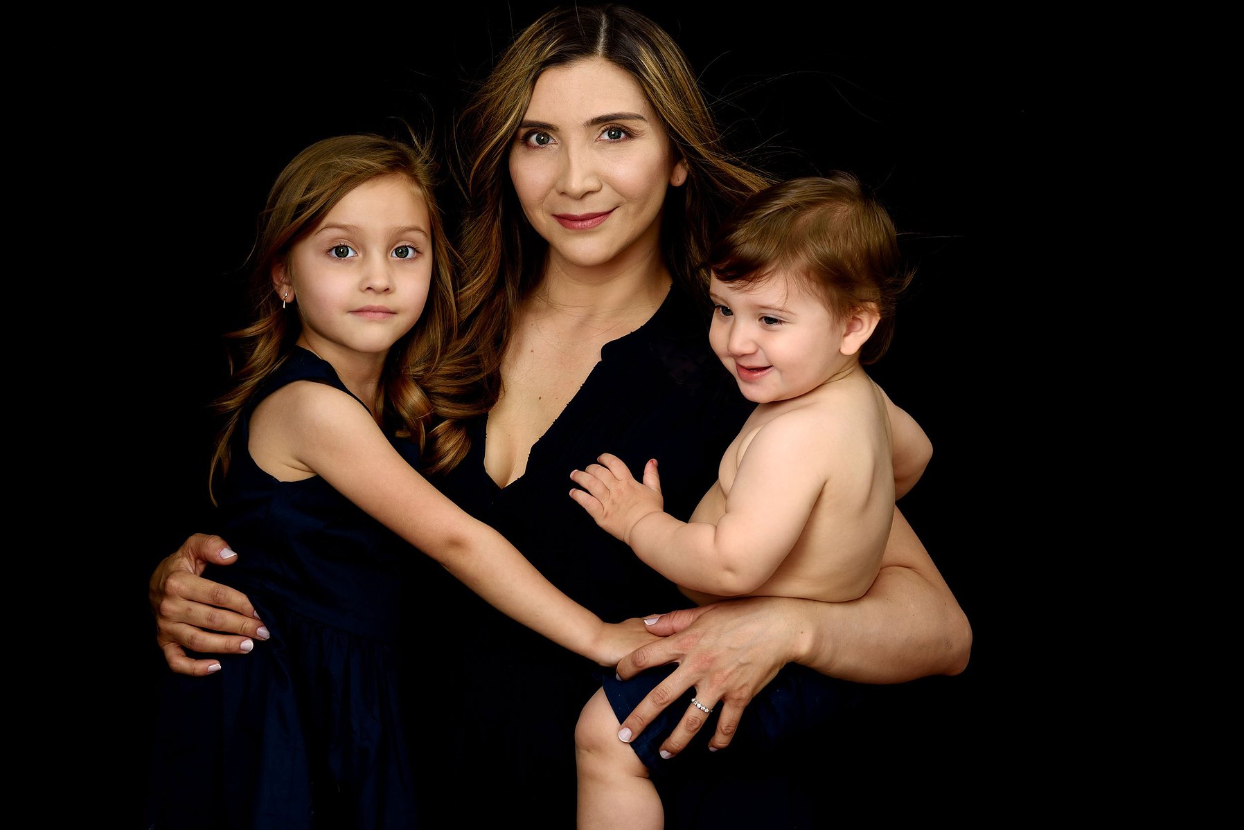 Fine-art Mummy and Me portrait, mother photographed with her daughter and her son on a black velvet background to celebrate Mother's Day.