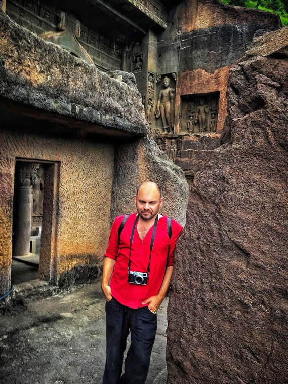 Travel Photographer Andrew Adams Poses in a red Kurta at the Ajanta Caves in Maharashtra, India. A Unesco world heritage site.