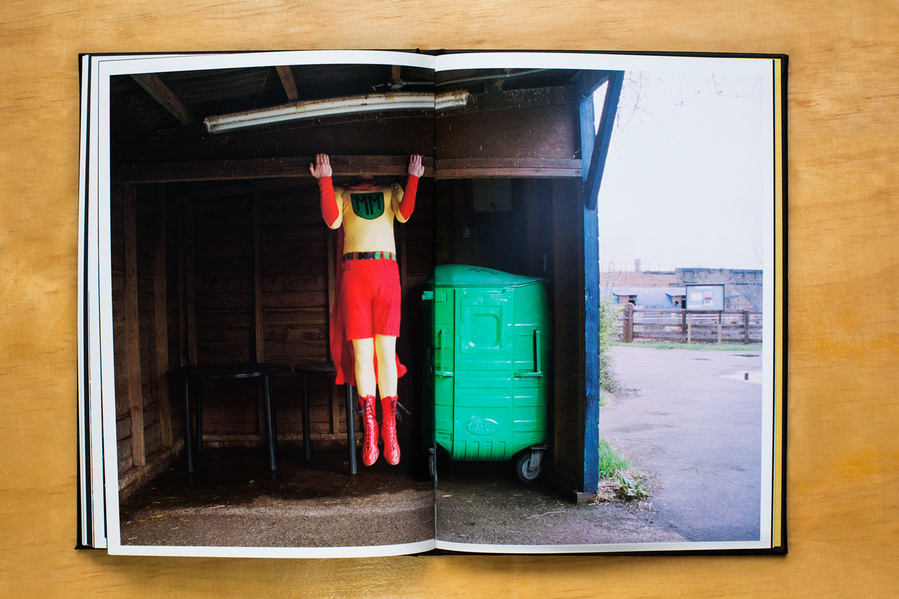 Superman's Pockets by Timothy Foster we see Mathsman performing a pull-up in a city farm London while wearing his costume coloured red & yellow leotard with a red cape.