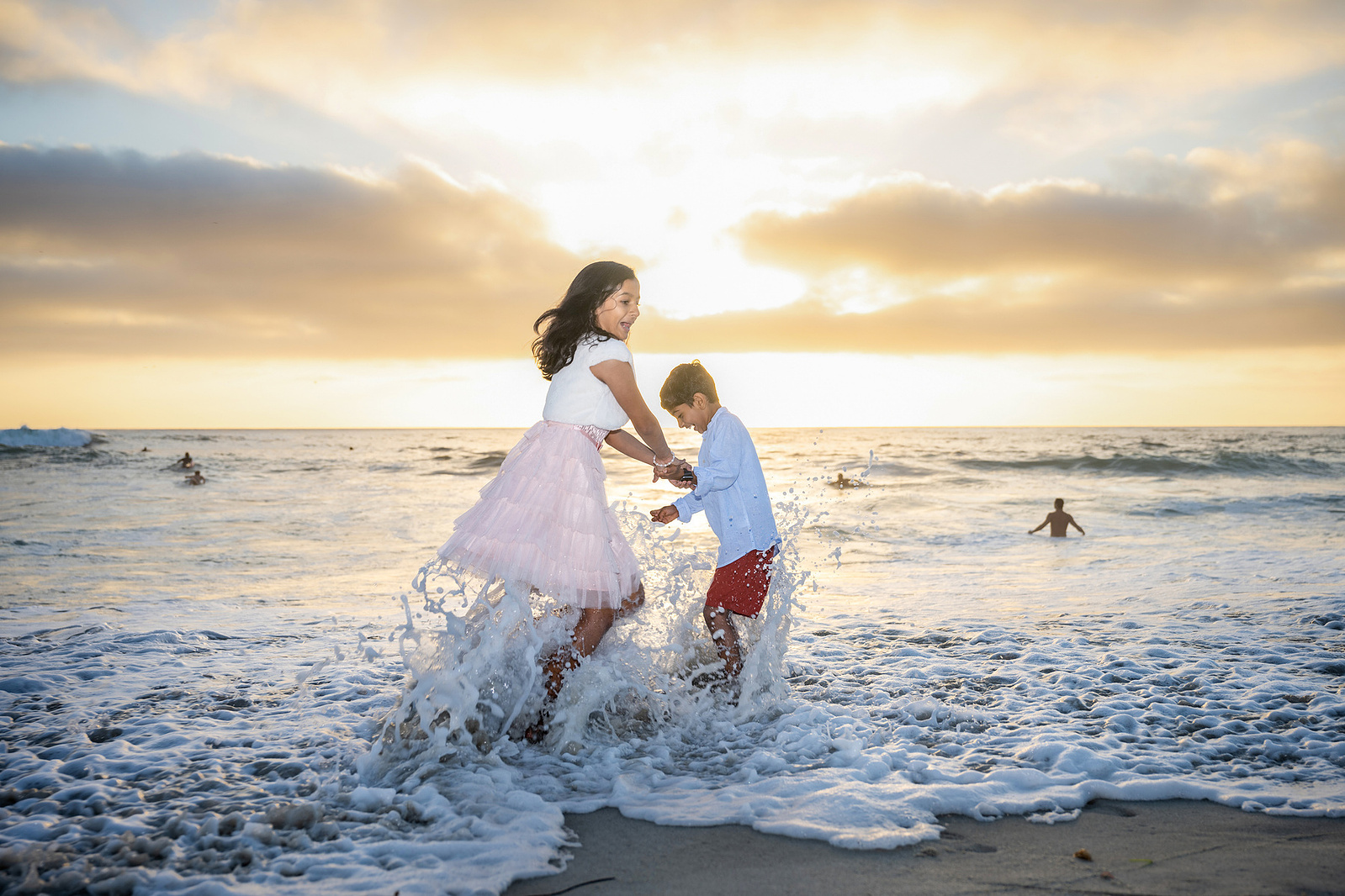 Brother and sister play in waves at sunset at Windandsea Beach in San Diego, California