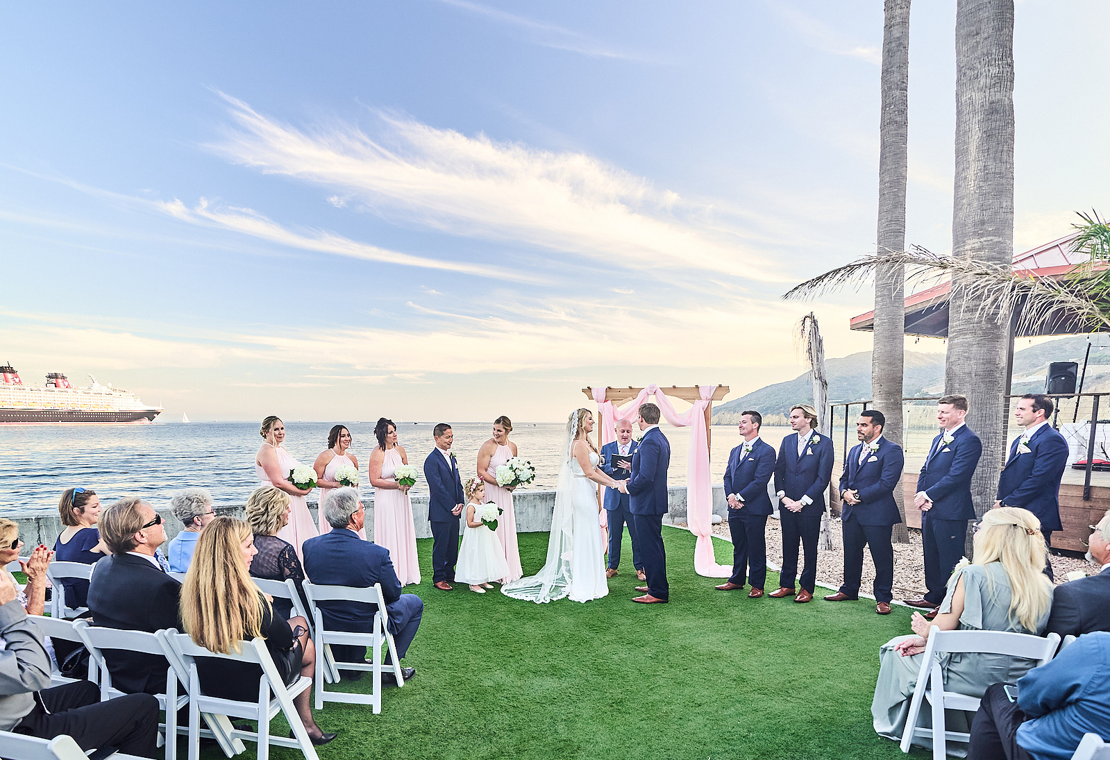 Bride and groom with wedding party during ceremony with San Diego Bay and a Disney cruise ship in the background.