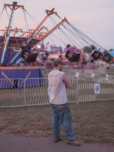 Man standing near ride at Prince William County Fair in the pink light of dusk.