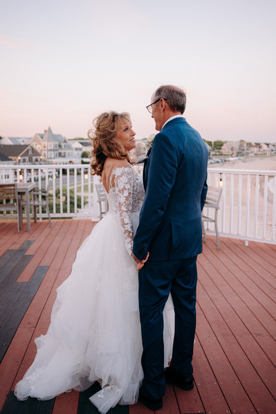 Bride and groom on balcony overlooking Falmouth in Cape Cod in soft pink dusk light.