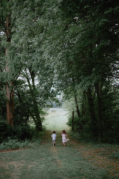 A young boy and girl walking through a tunnel in the green trees.