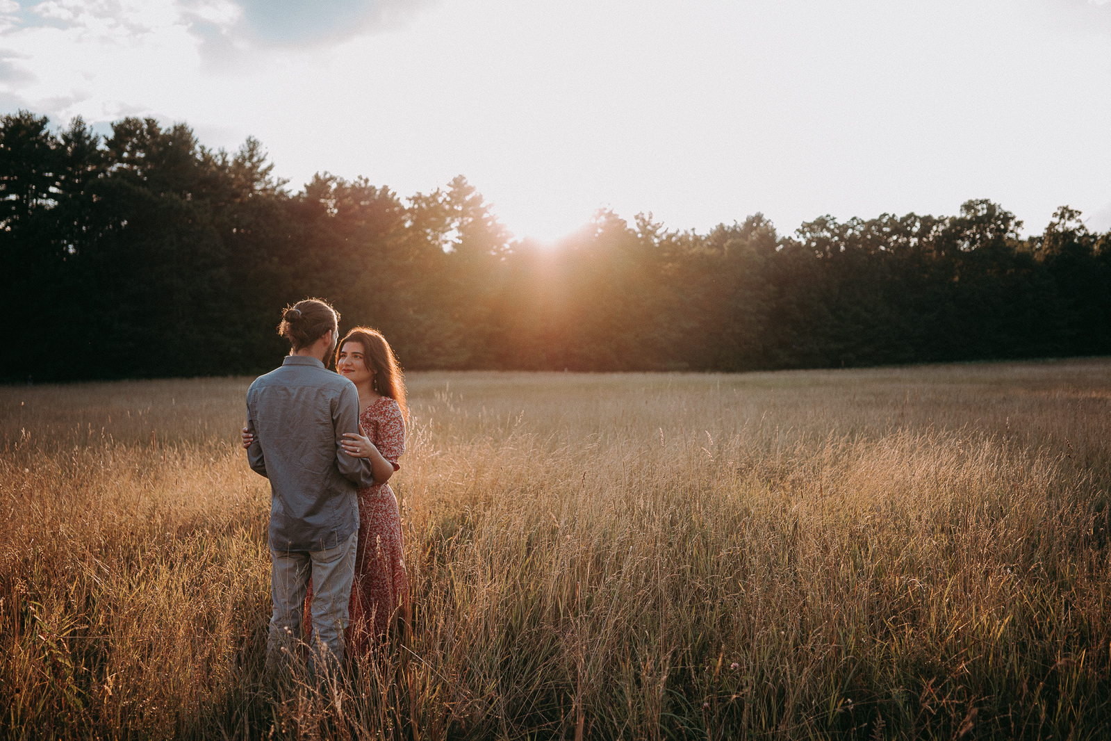 Golden-hour engagement session in grassy field during sunset.