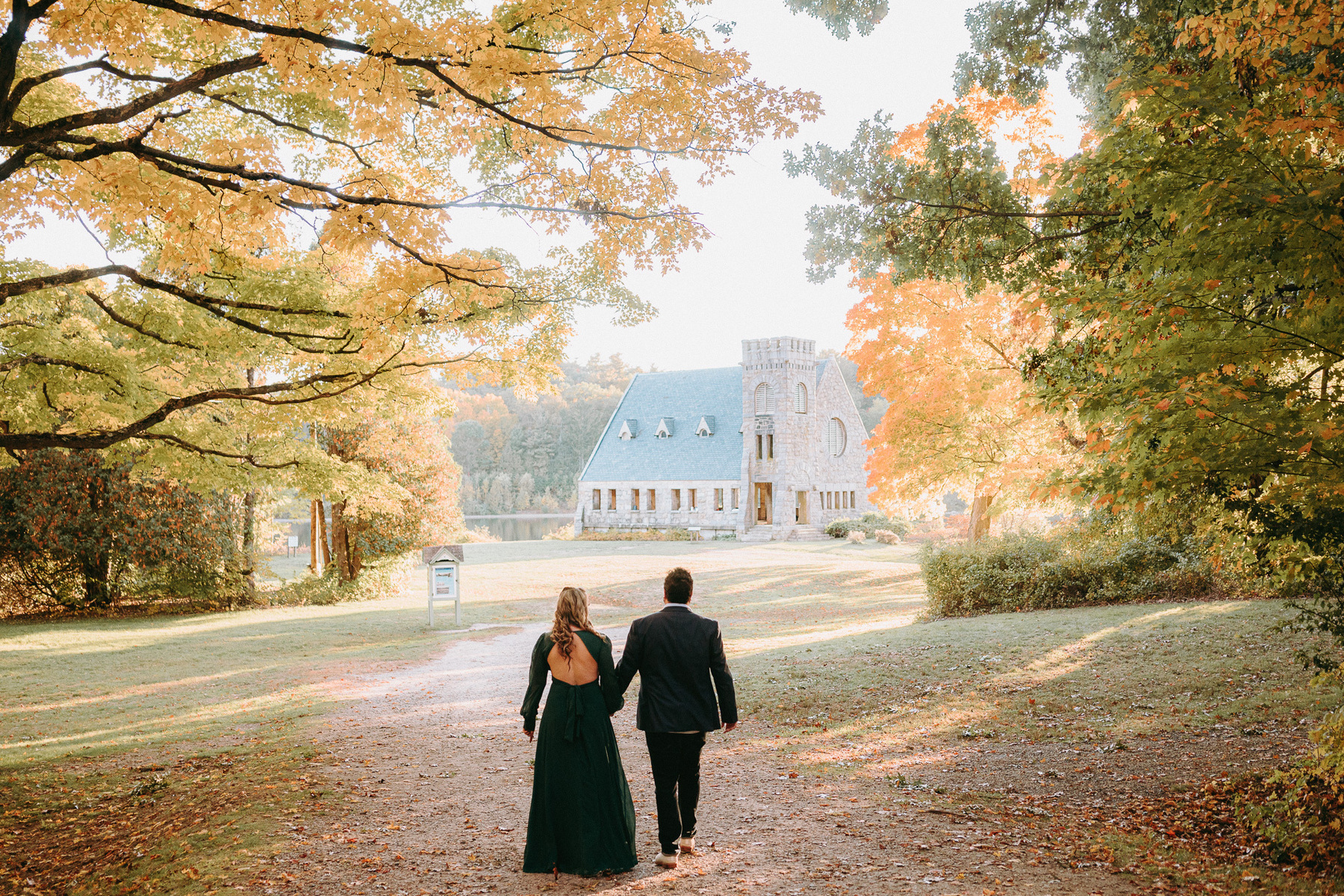Engaged couple holding hands, surrounded by fall foliage at Old Stone Church in West Boylston.