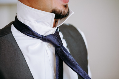 Details of groom putting on purple tie.