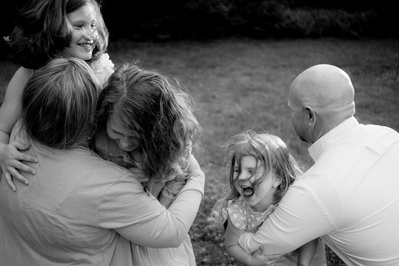 Mother and father hugging laughing young daughters in black and white.