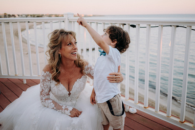 Bride hugging grandson ringbearer at Cape Cod beach wedding reception in soft golden hour light.