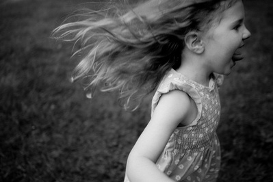 Toddler girl running with her hair blowing wildly in black and white.