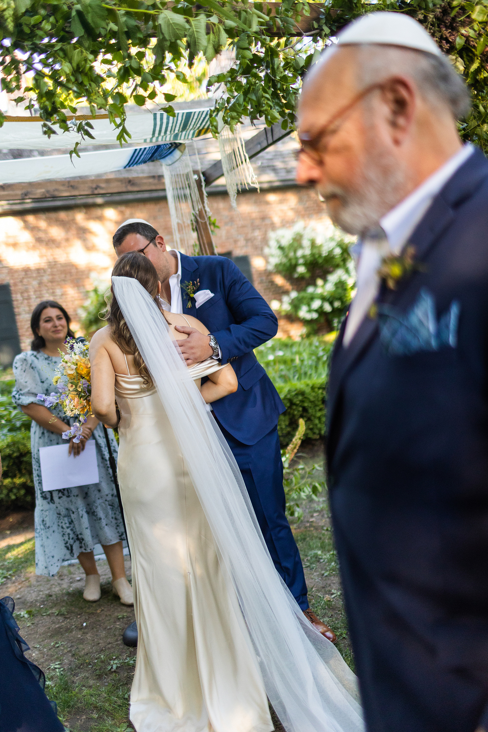 Bride and groom greet each other and Father of the bride walks in foreground. Wedding photojournalism at Senate Garage in Kingston, NY.