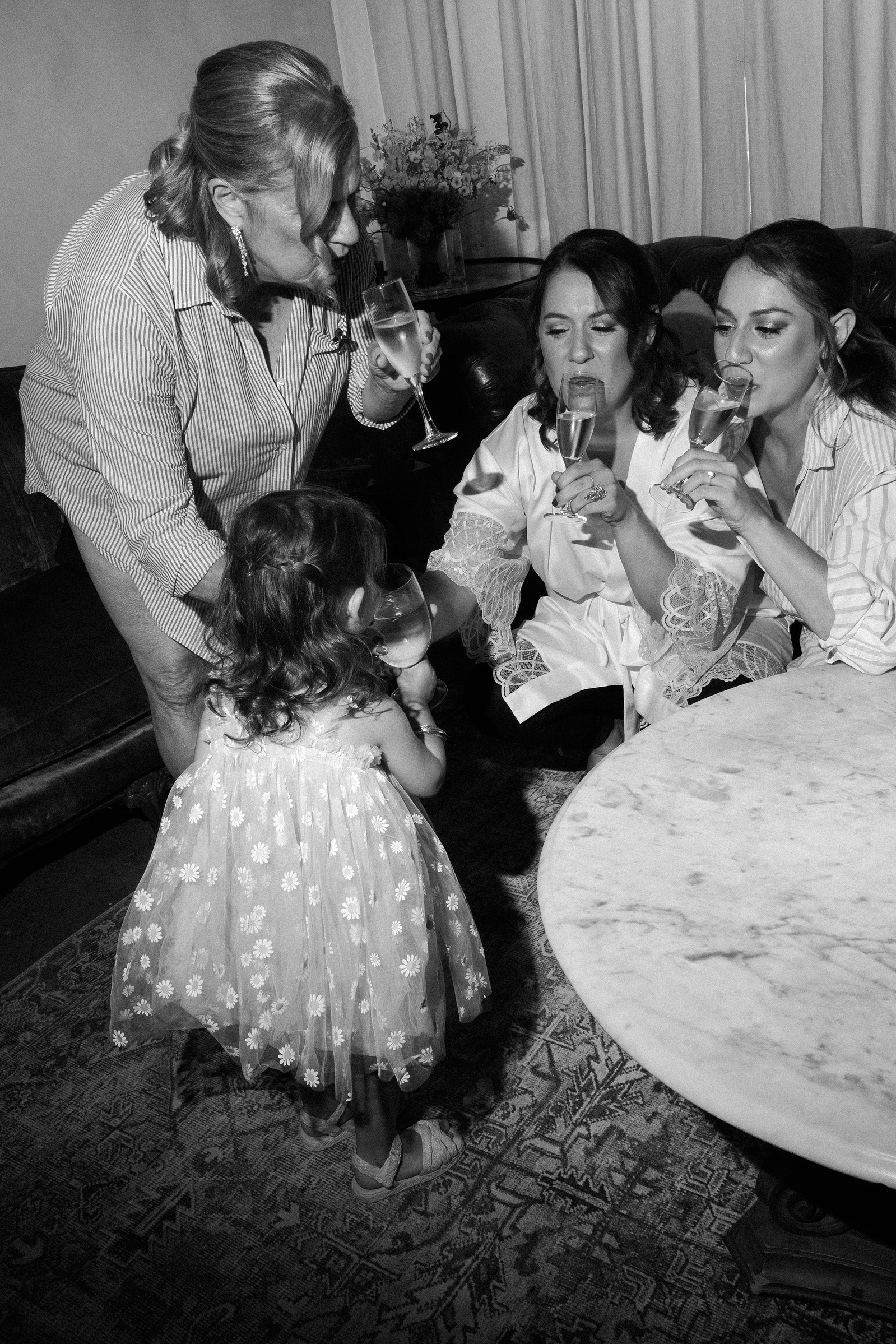 Mother of the bride, bride, sister of the bride and flower girl cheers. Black and white. Wedding photojournalism at Senate Garage in Kingston, NY.