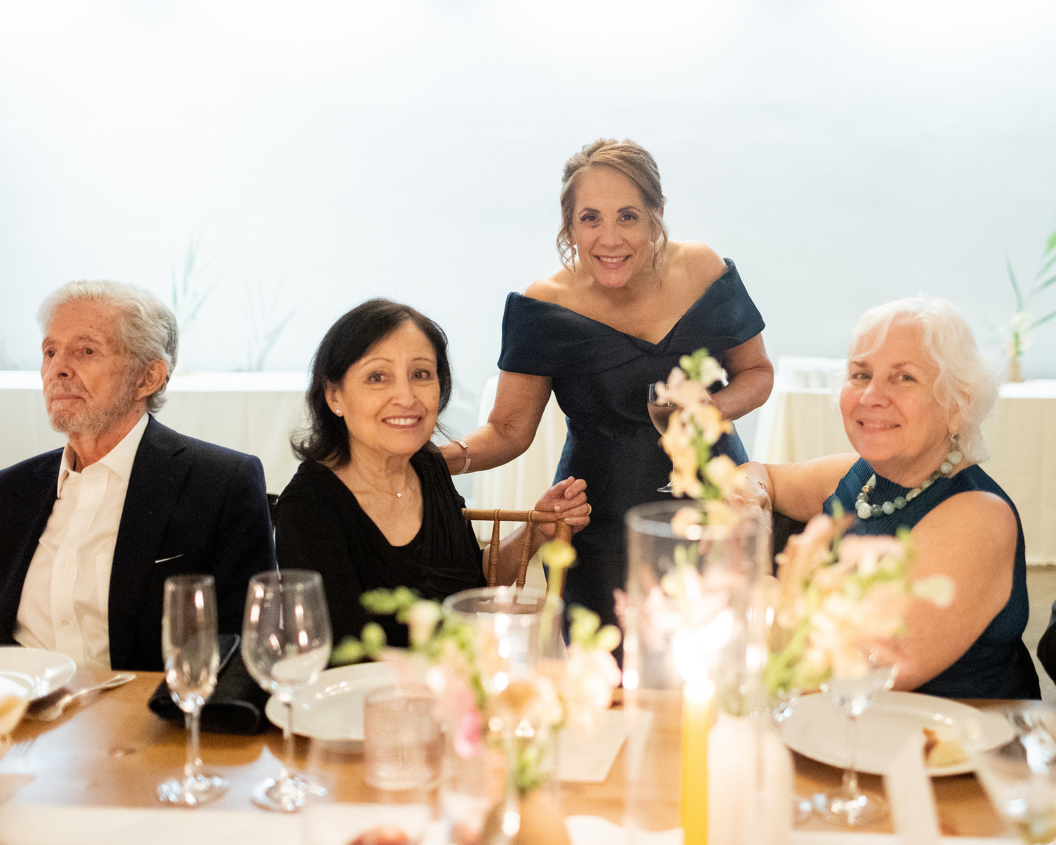 Mother of groom speaks with three guests at candle lit dinner. Wedding photojournalism at Senate Garage in Kingston, NY.
