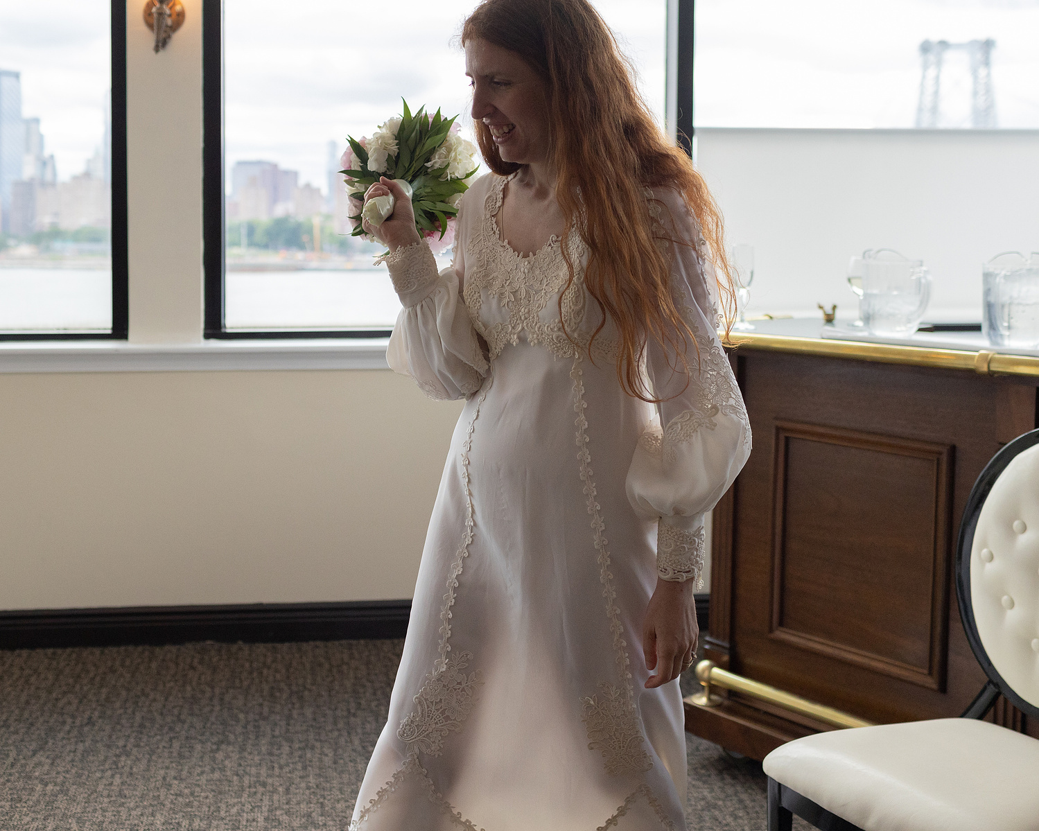 Bride walks across room, light streams through dress to show shape of her legs as she walks. Wedding photojournalism at Giando on the Water in Brooklyn, NY. 