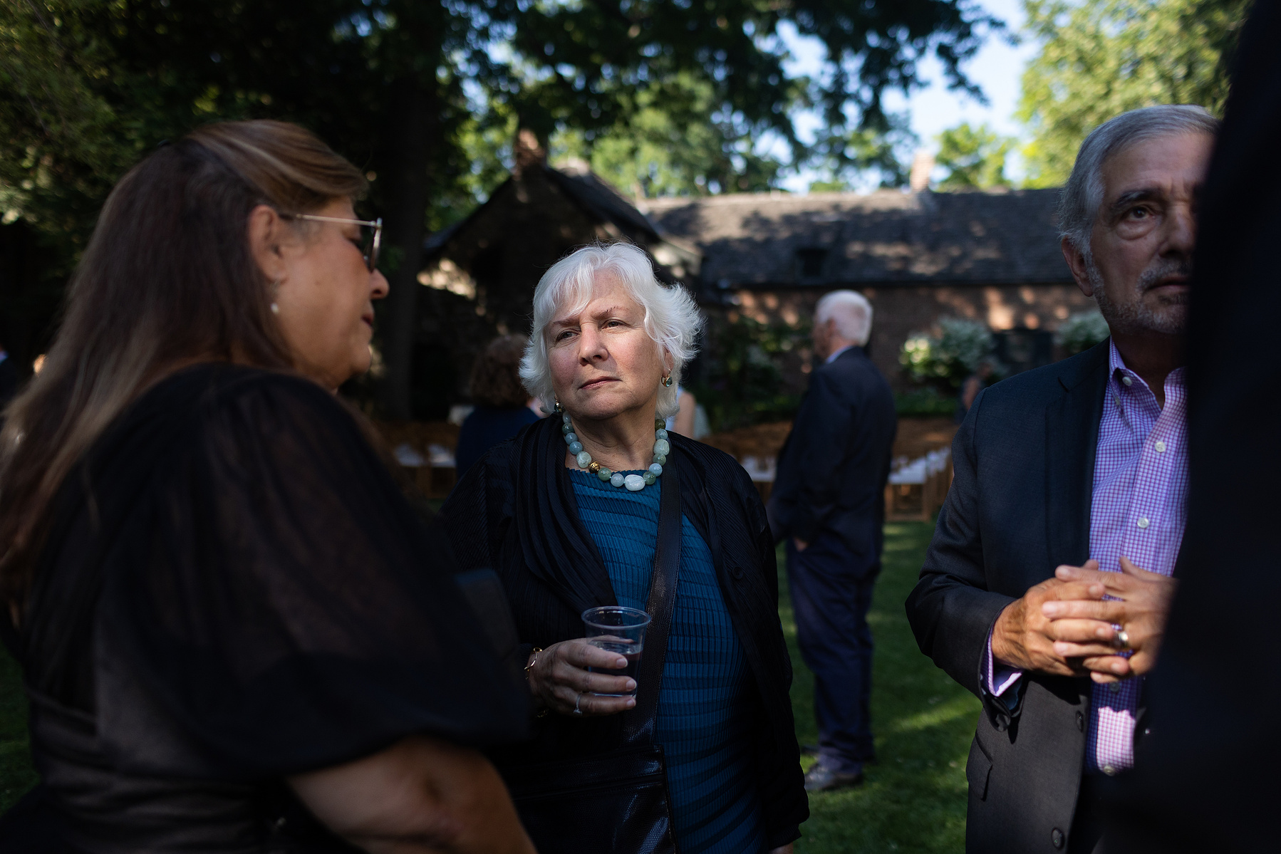 Wedding guests stand in dappled sunlight at cocktail hour. Wedding photojournalism at Senate Garage in Kingston, NY.