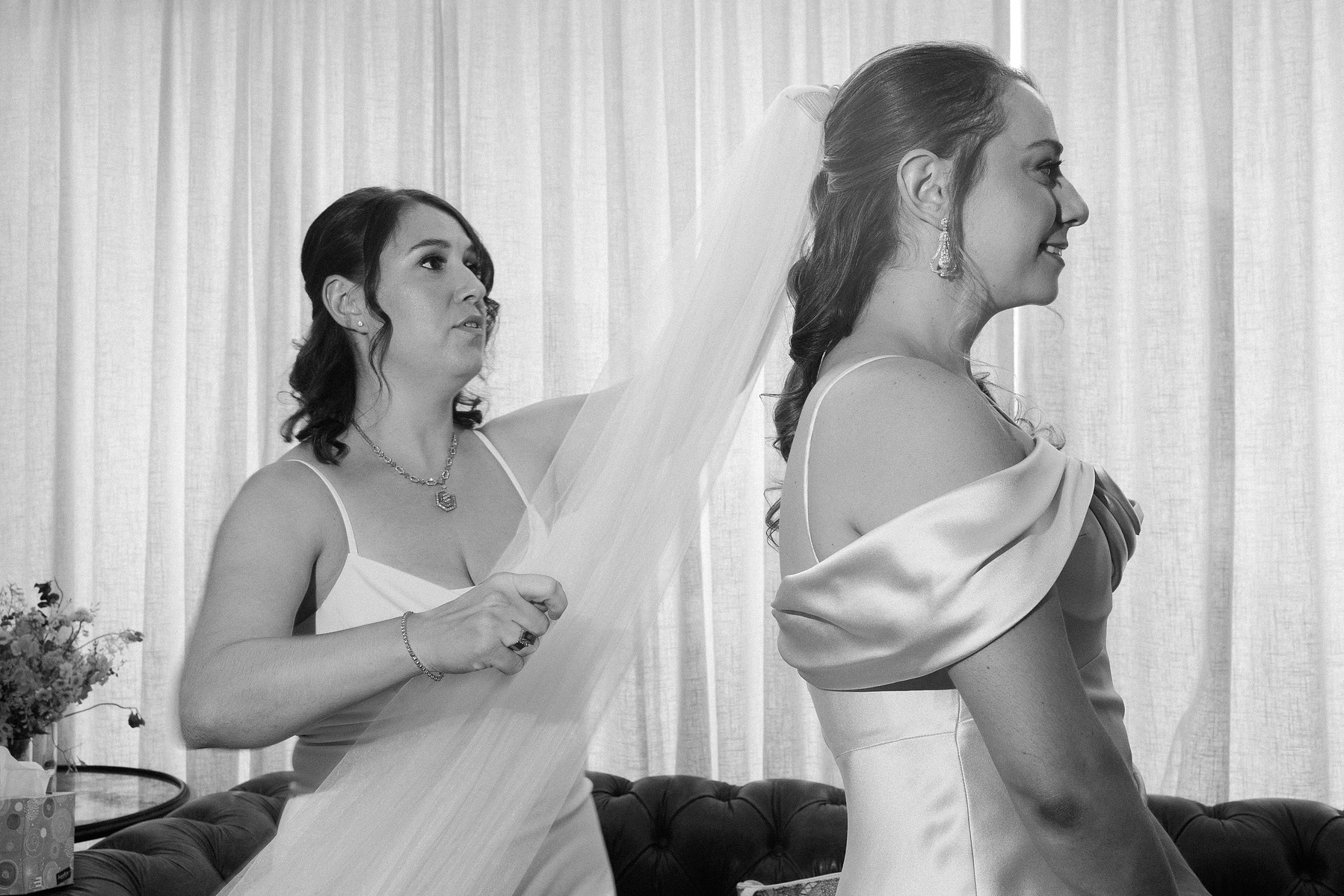 Sister puts veil on bride. Black and white. Wedding photojournalism at Senate Garage in Kingston, NY.