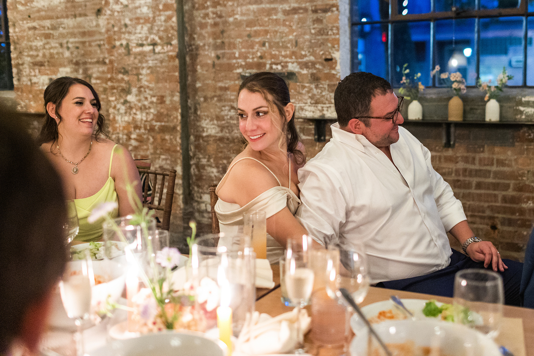 Bride holds groom at table during speeches. Wedding photojournalism at Senate Garage in Kingston, NY.