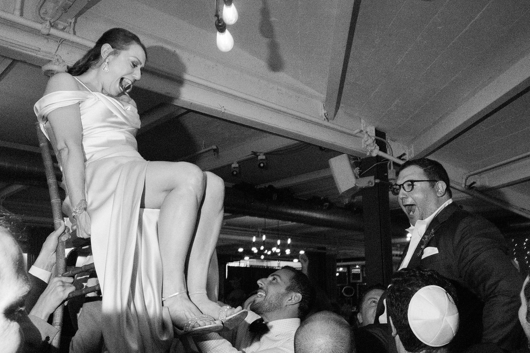 Bride and Groom get lifted in chairs during the hora. Wedding photojournalism at Senate Garage in Kingston, NY.