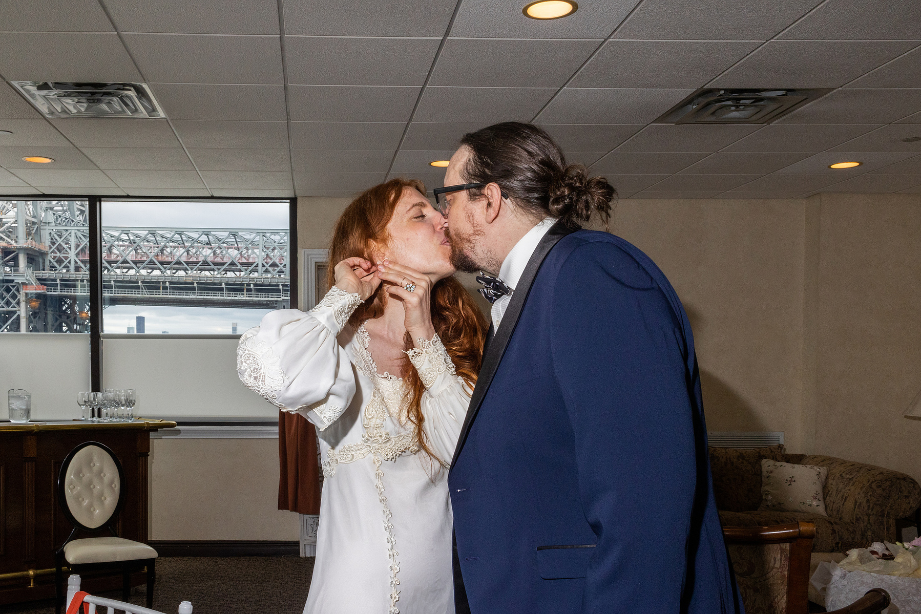 Bride and groom kiss while getting ready. Bride is putting on earring. Wedding photojournalism at Giando on the Water in Brooklyn, NY. 
