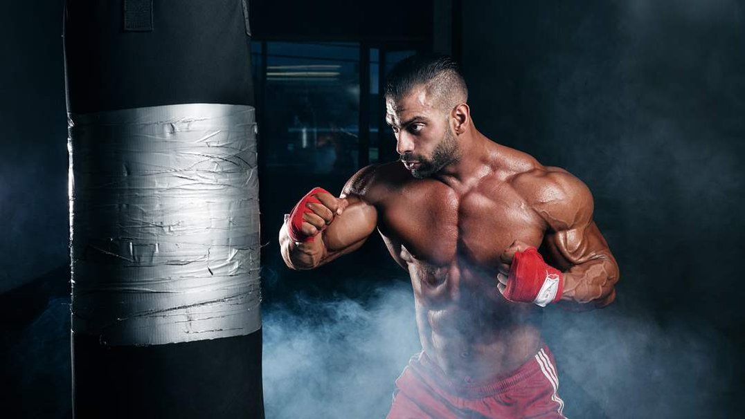 Muscular Bodybuilder with boxing wraps and a punching bad