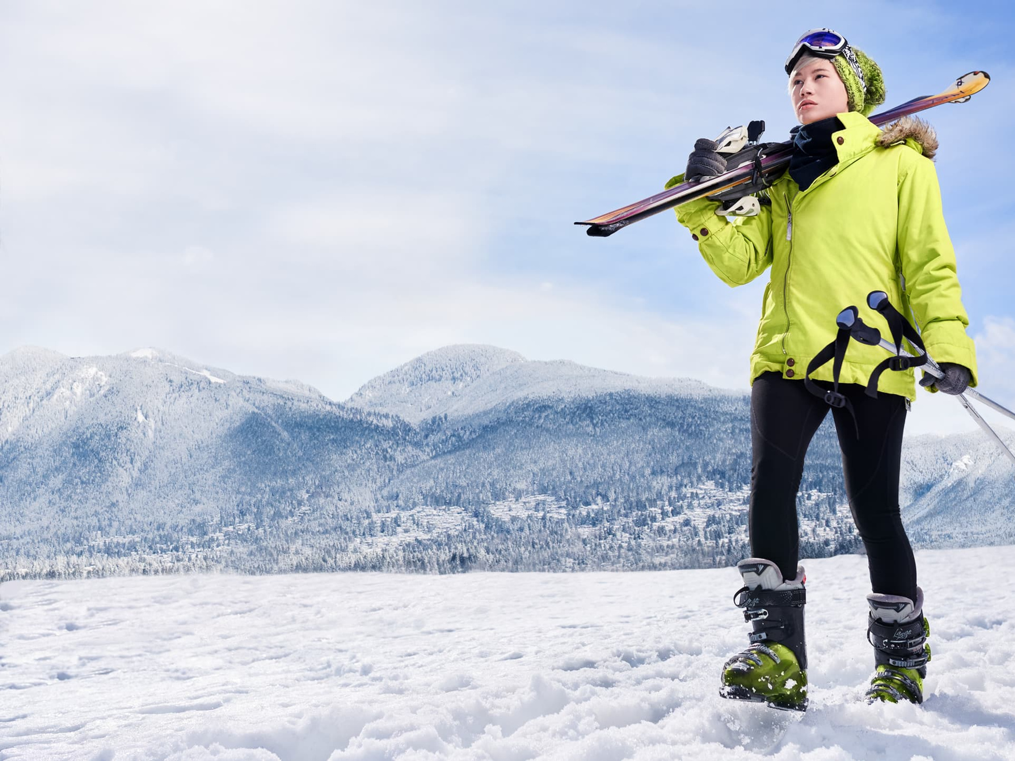 Woman in a snow suit holding skis walking behind a mountain range