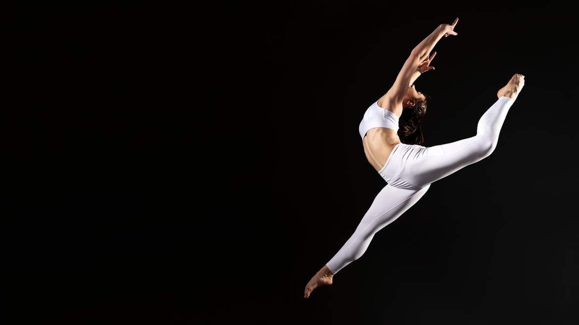 Ballerina dressed in white activewear jumping and performing a grand jeté ballet jump