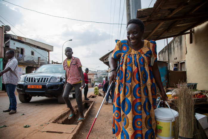 Marie Madelaine is the training leader for the cocoa butter making workshop which is taking place at Eveline's home. In the picture she is coming out from a shop where the cocoa beans were grinded. Marie Madeleine has been blind since the age of five. Aft