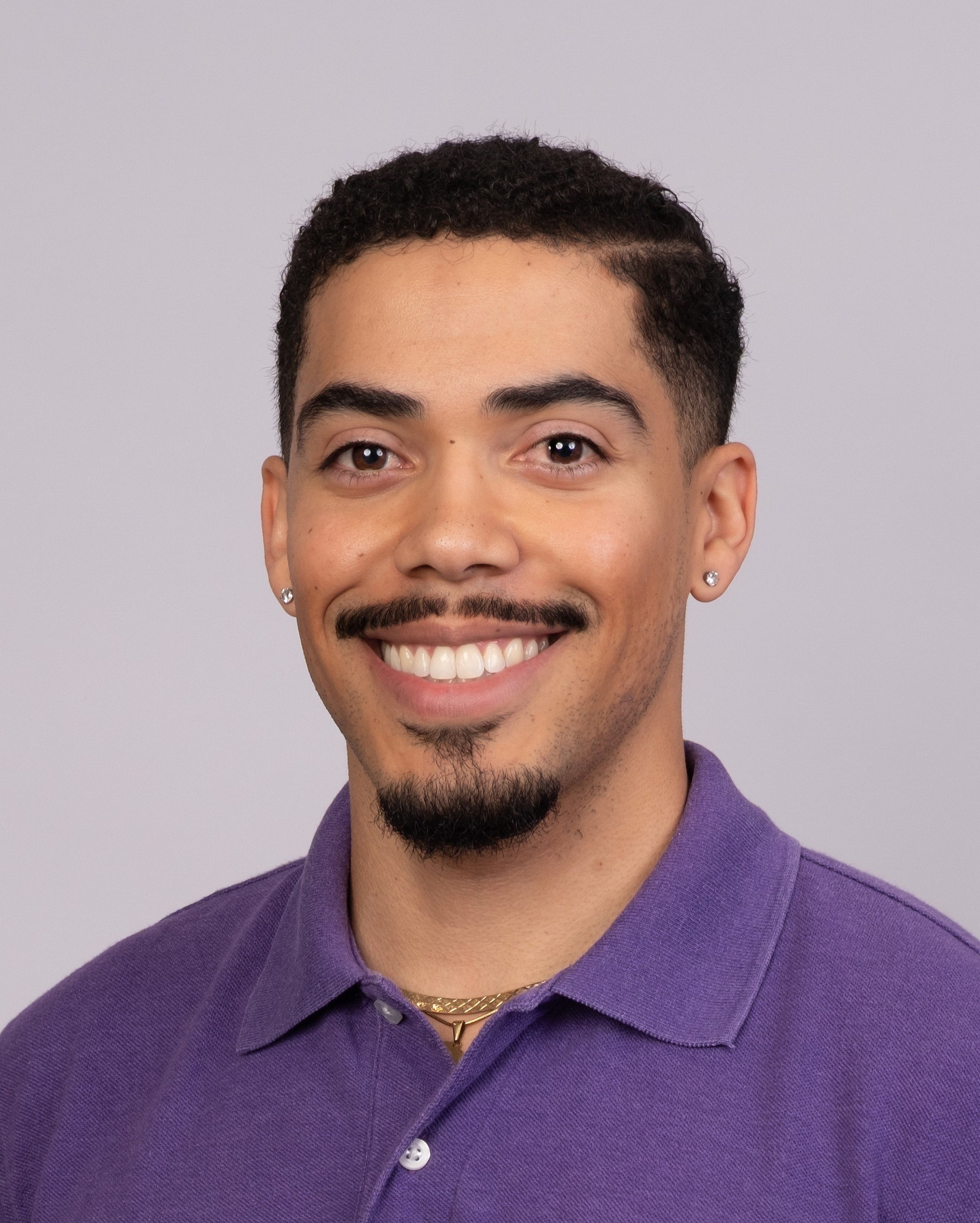 Professional Headshot and Profile Photo of handsome racially ambiguous man (Matthew J. Sanchez, Perfumer & Founder of MATTEO PARFUMS) smiling, wearing a purple polo shirt, with a gold necklace