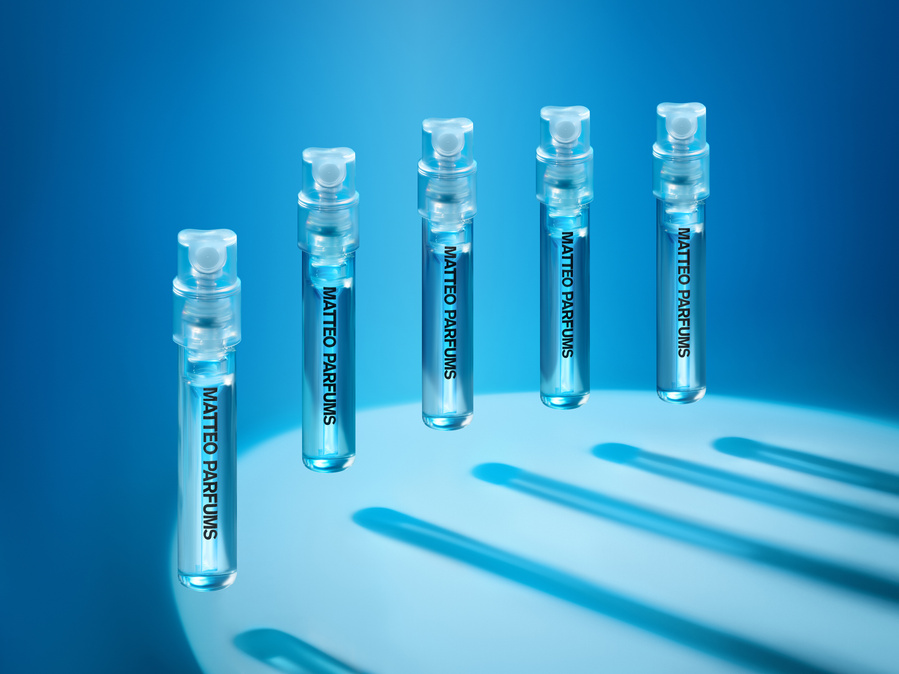 Five floating vials of MATTEO PARFUMS Lovers' Dew (sample size, 2ml), a modern and fresh aquatic fougère scent against various beautiful water blue colors, lined up in a crescent-shape