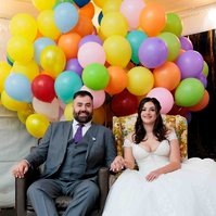 man and woman sitting in brown chair and floral chair in front of balloons inspired by the movie Up