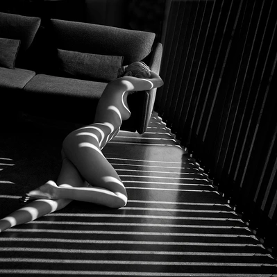 A nude woman, bathed in the stark light of a sunlit room, stretches languidly on the floor.  Shadowy lines accentuate her form.