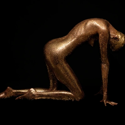 A figure, draped in shimmering gold, kneels in a posture of vulnerability.