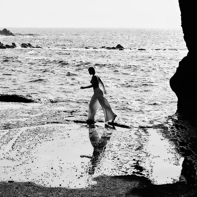 Reflections dance on the water's edge as a figure walks along the shore.