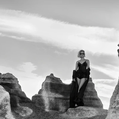Silhouette against a sculpted landscape; a woman stands resolute, her form a stark contrast to the rugged terrain.