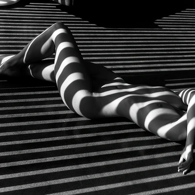 Photo from a body lying in the sand, sculpted by light and shadow, rests on a rhythmic grid of lines.
