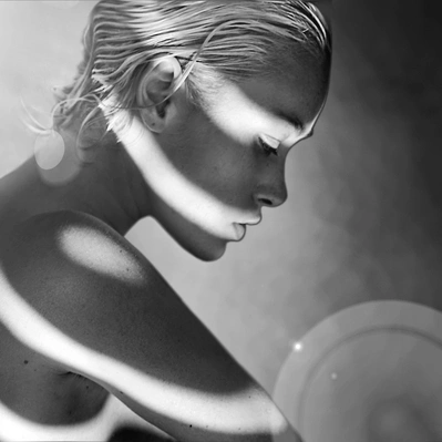 Soft light sculpts a woman's face and body, highlighting her delicate features.