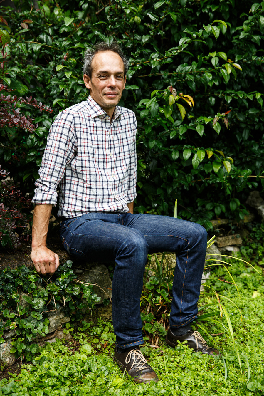 Davide Uglietti a physicist living in Switzerland sits in the lush green garden of his house. Portrait for the Financial Times.